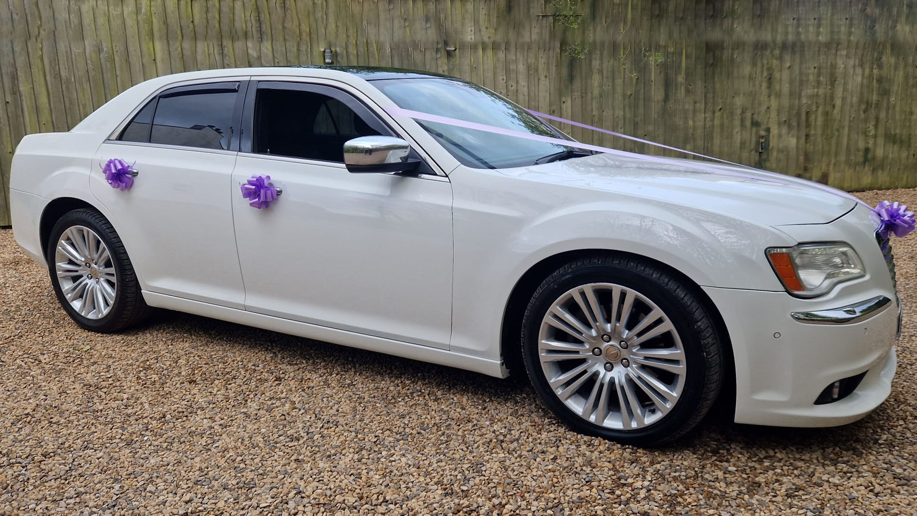 Right side view of a White Chrysler 300c car with Purple ribbons and bows on the door handles