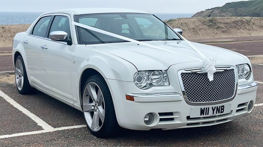 White Chrysler 300c Saloon Car with white wedding ribbons parked by the sea side in Durham