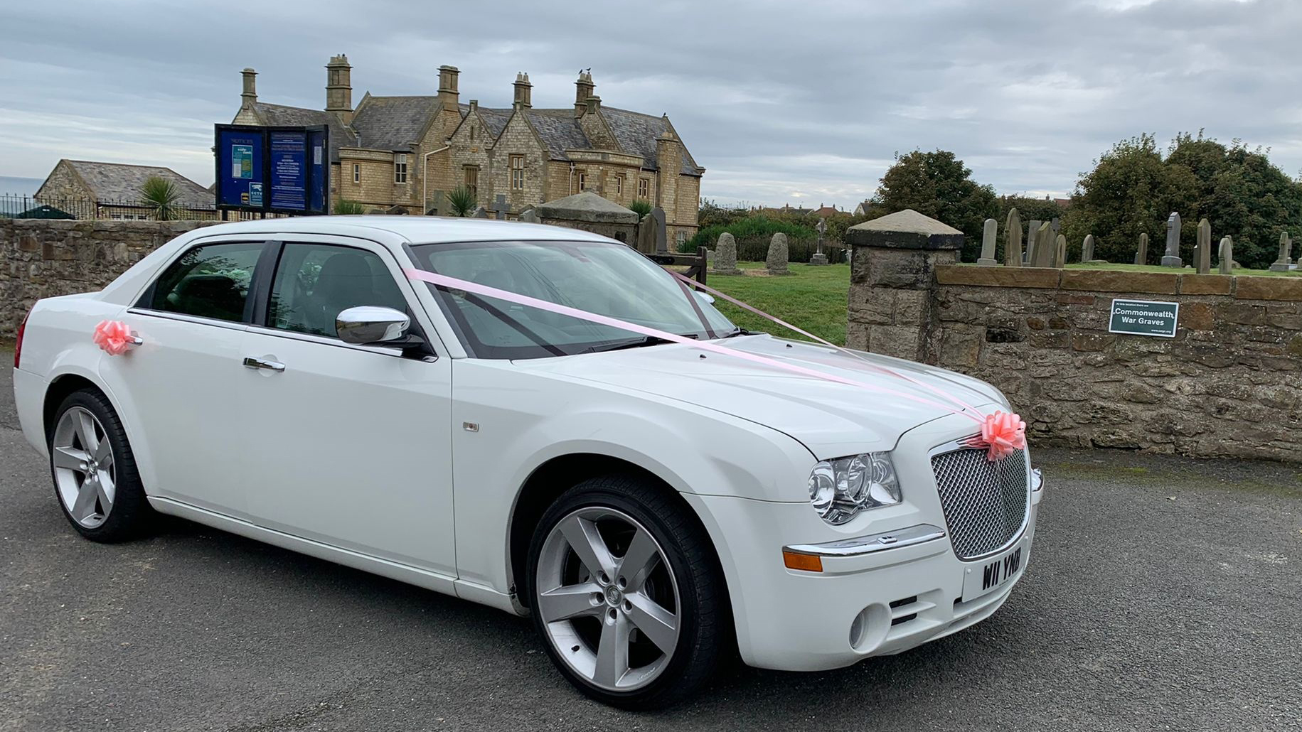 White Chrysler 300c Saloon Car decorated with wedding ribbons in front of a church