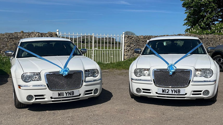 Two identical White Modern 300c saloon cars dressed with matching blue ribbons parked next ot each others