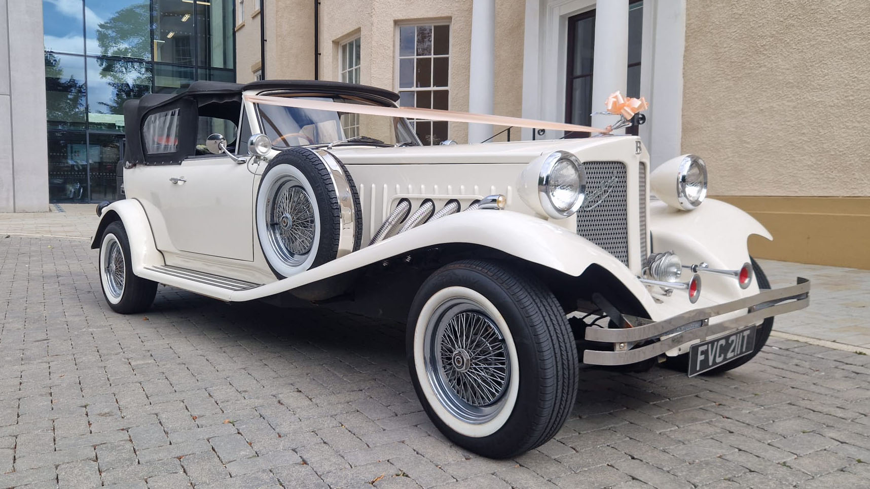 Cream vintage style Beauford with black soft top roof closed and decorated with light orange ribbons and bows