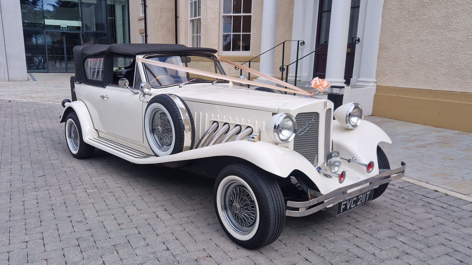 1930s vintage style Beauford convertible in cream with black soft top roof and white wall tires.