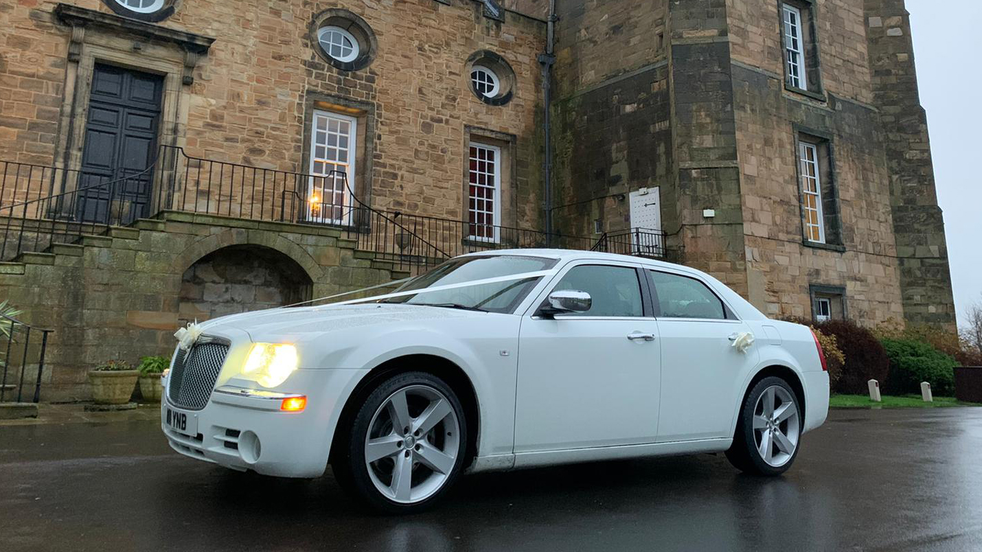 White Chrysler 300c Saloon Car in front of a wedding venue in Durham with headlights on