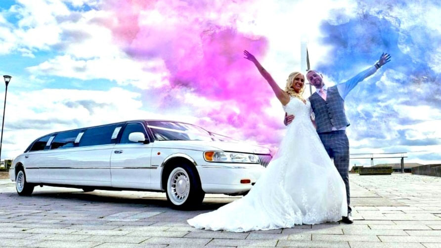 Bride and Groom standing in front of a White Stretched limousine with blue and pink smoke flair in the background