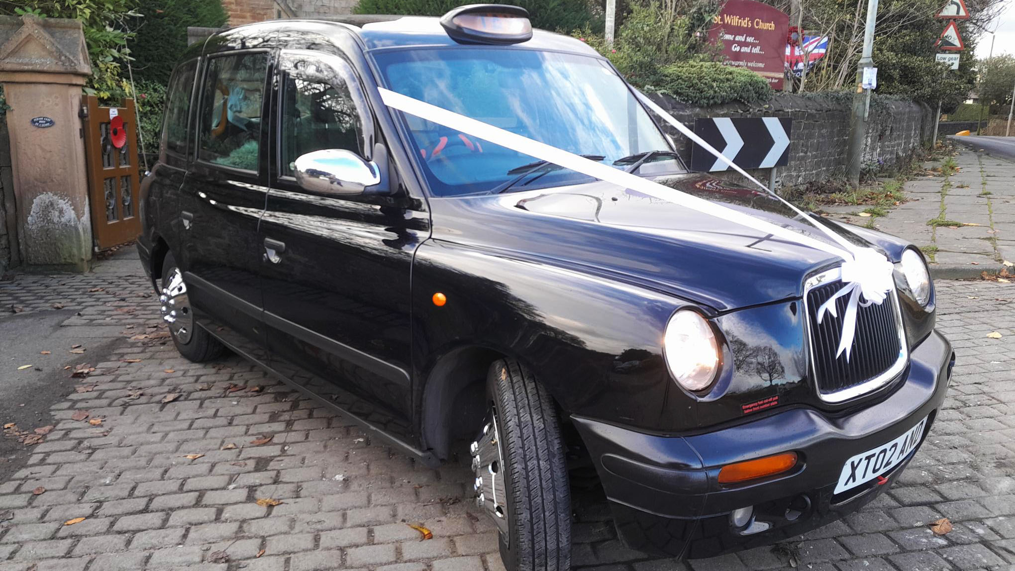 Front right view of a modern Black Taxicab decorated with white ribbons