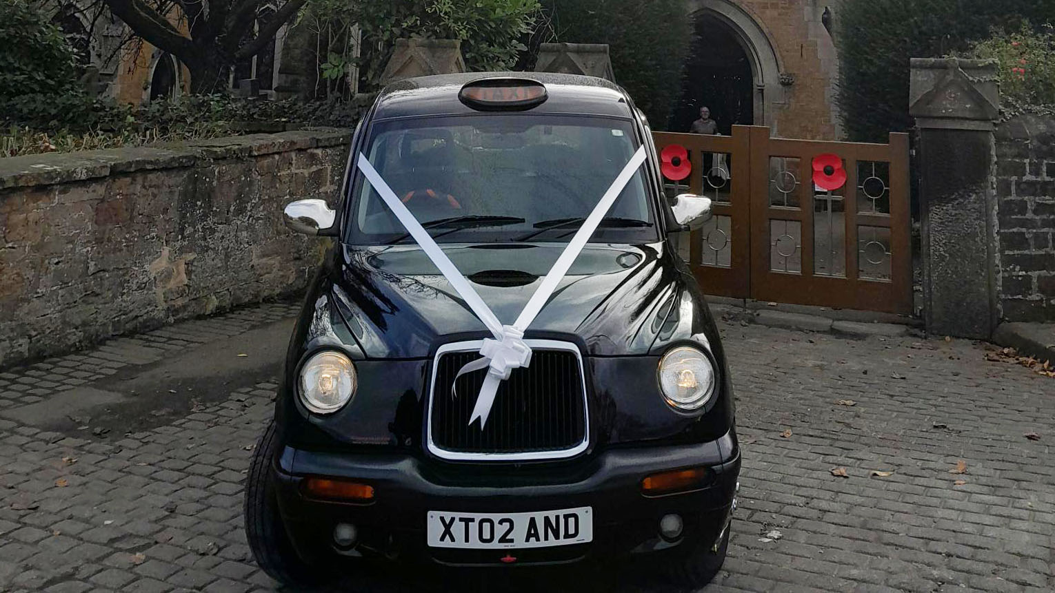 Front view of black taxi cab with white wedding ribbons and headlights on