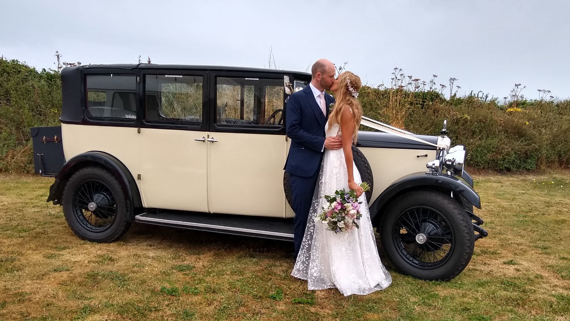 Bride and Groom kissing in front of a vintage car in Cream and Black