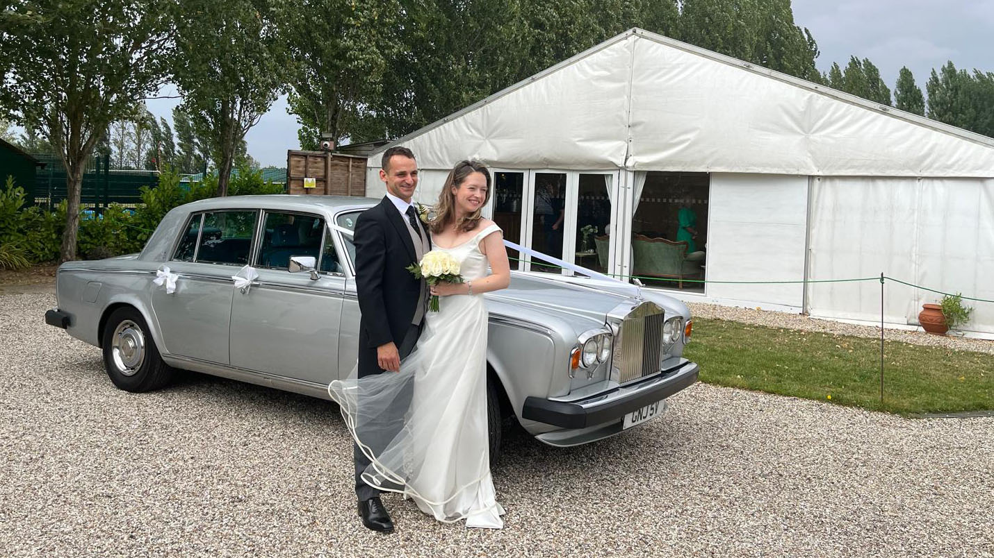 Bride and Groom with a classic Rolls-Royce Silver Shadow dressed with white ribbons and bows in the background