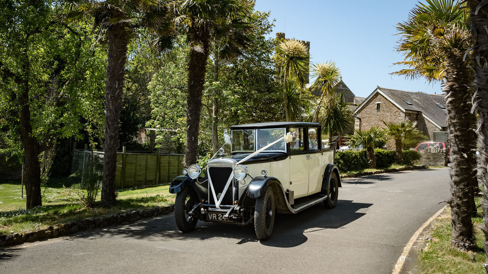 Vintage daimler in Black and Cream decorated with wedding ribbons leaving a Devon wedding venue