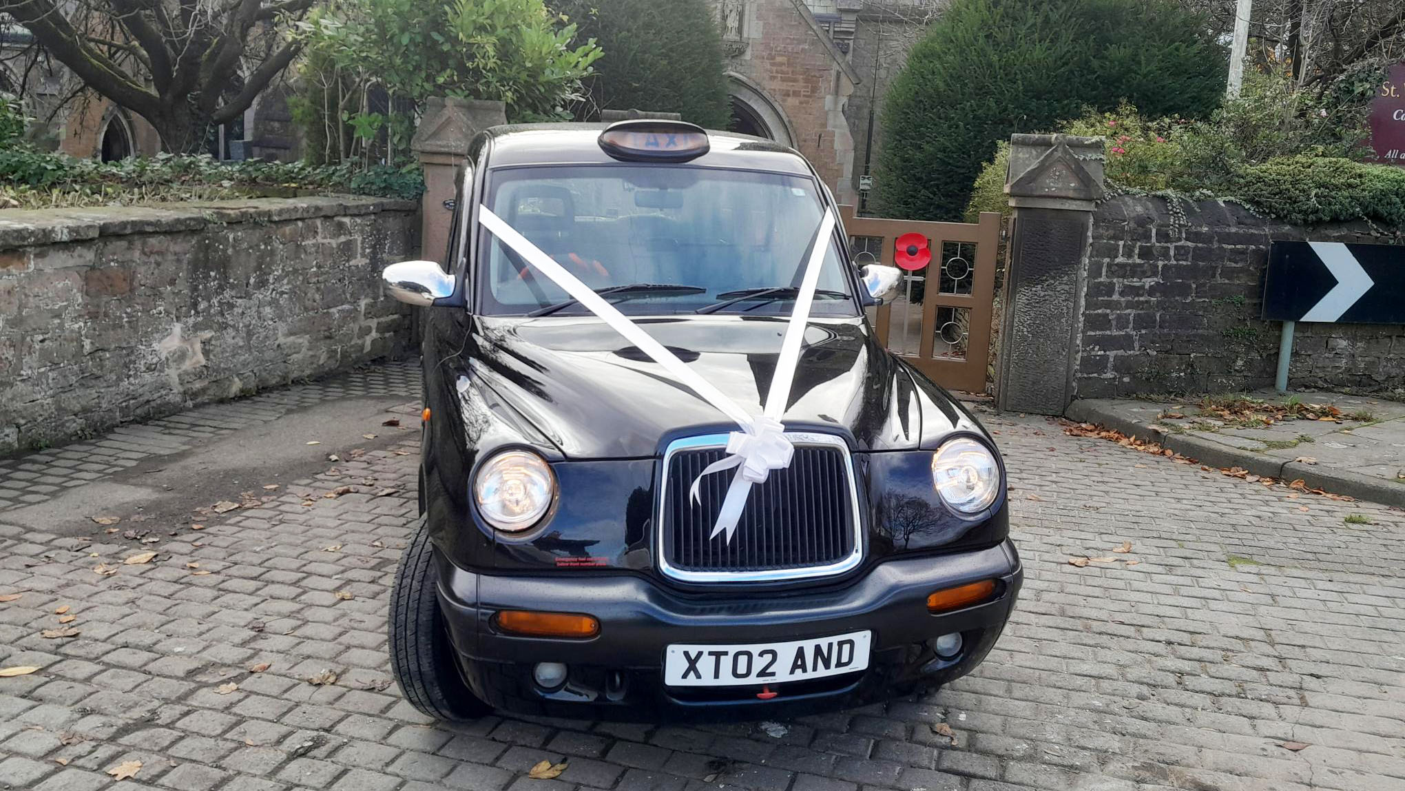 Front view of black taxi cab with white wedding ribbons parked in frotn of Church's wooden gate