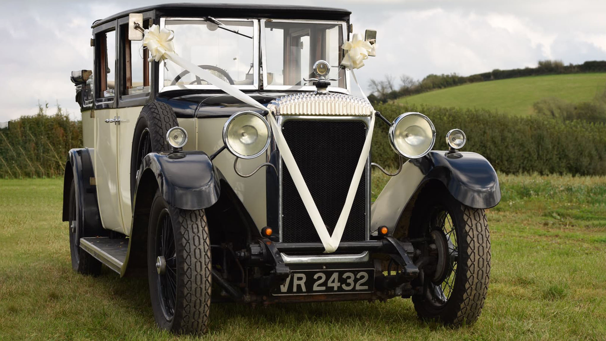 Frotn view of Vintage Car decorated with white ribbons parked in a green field