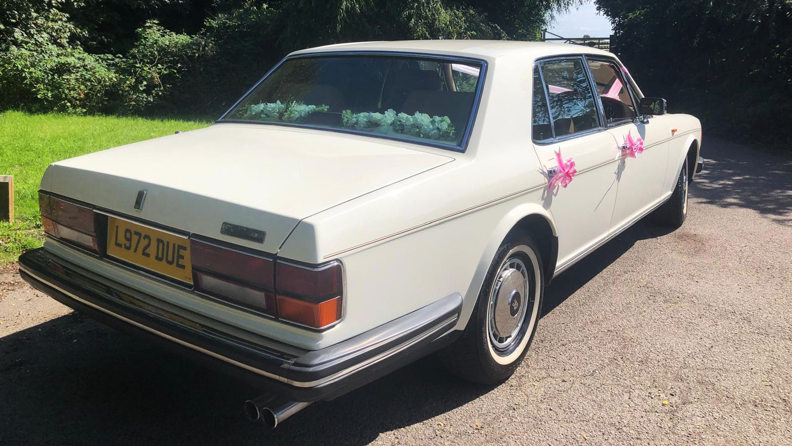 right rear view of classic Rolls-Royce Silver Spirit decorated with pink ribbons and white flowers on parcel shelf