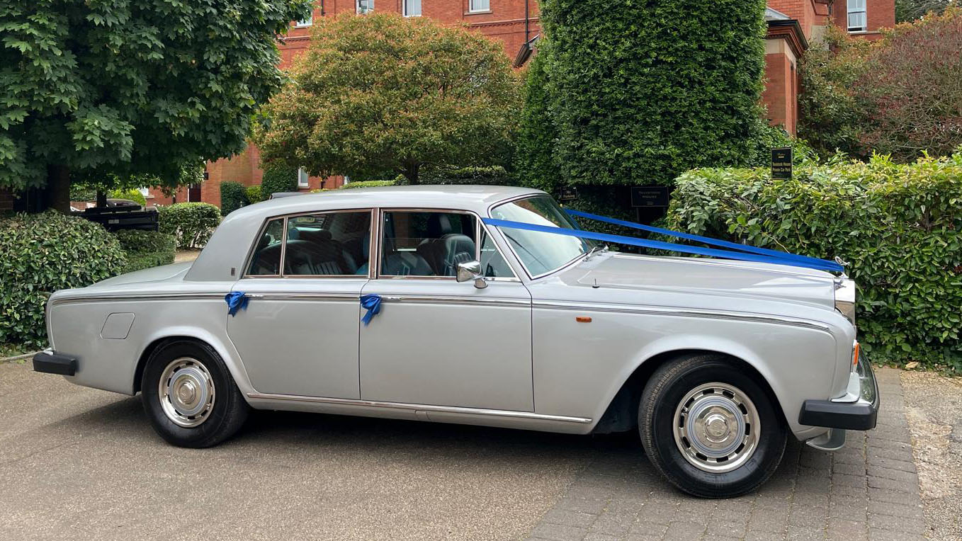 right side view of a classic Rolls-Royce Silver Shadow in silver dressed with royal blue ribbons