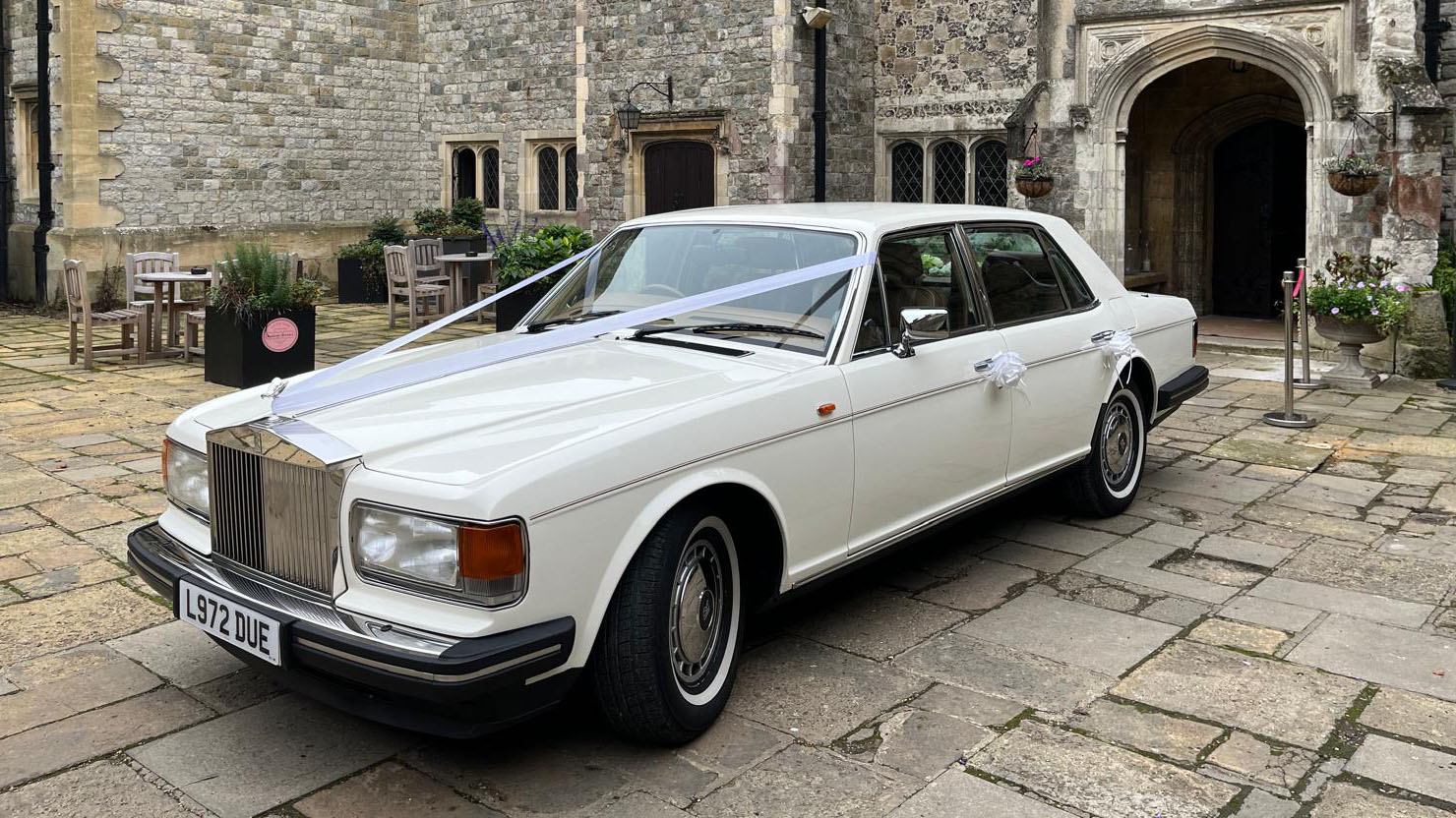 White Rolls-Royce Silver Spirit decorated with wedding ribbons in front of wedding venue in Essex