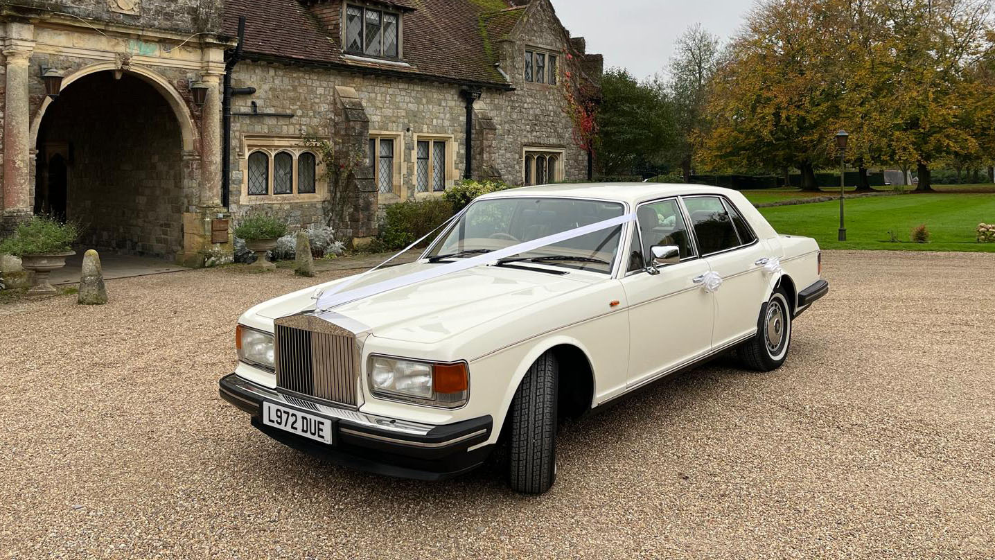 white classic Rolls-Royce Silver Spirit with weding ribbons in front of a wedding venue in Essex