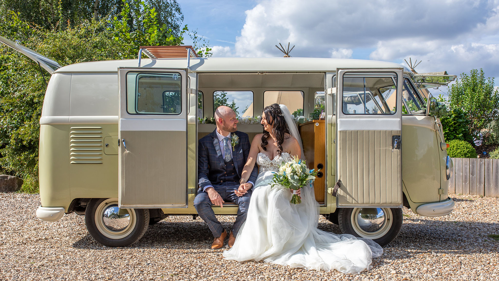 Bride and groom seating on the rear step of a classic campervan