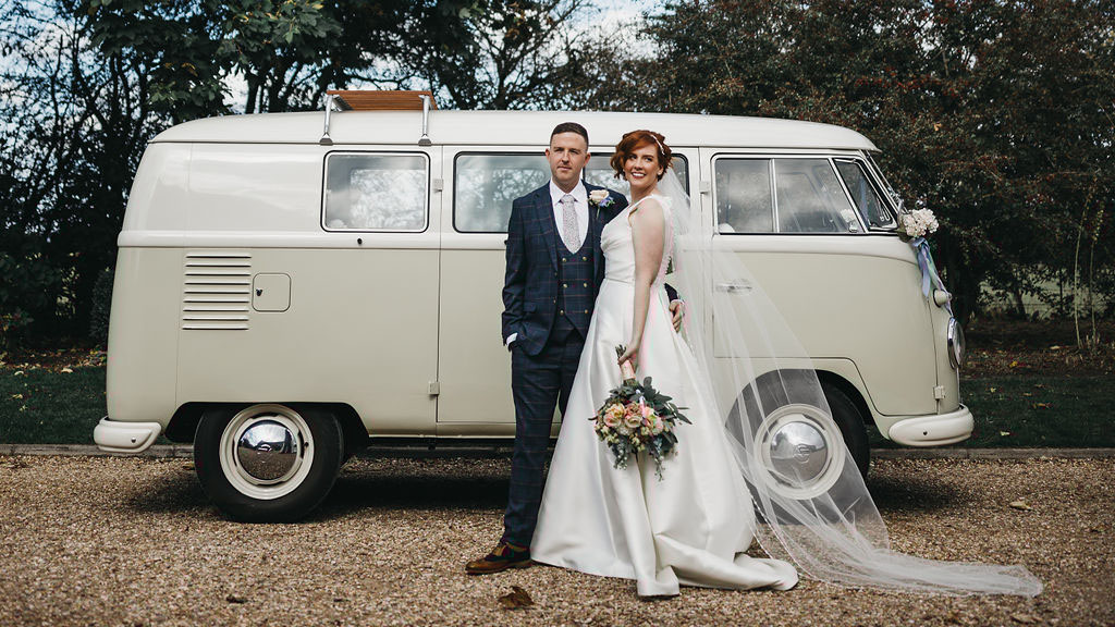 Bride wearing a white dress standing with her groom in front of a classic campervan