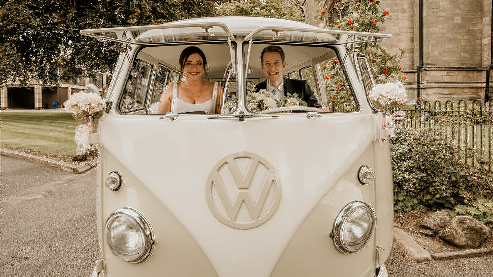 Bride and groom seating in the front seat of a classic campervan with both front splitscreen windows open