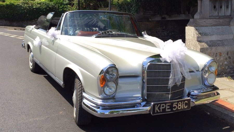 Classic Silver Mercedes se220 with soft top convertible roof down and decorated with white ribbons and large white bows