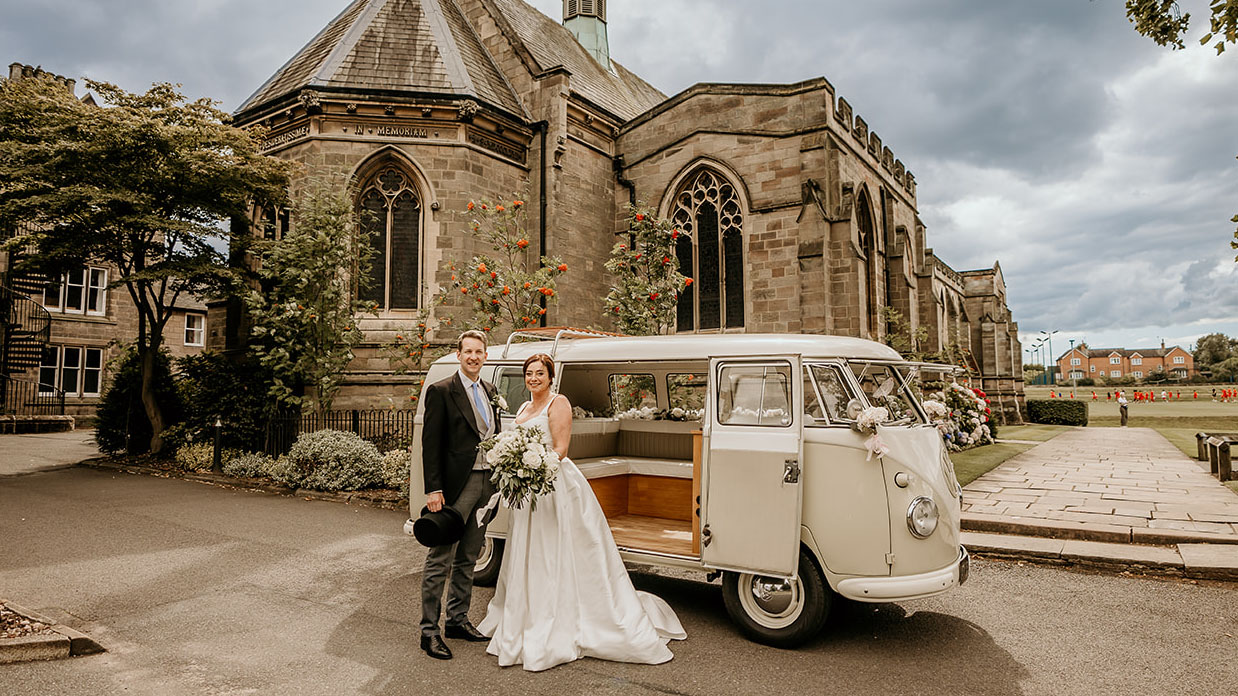 Bride and groom with a classic campervan and church in Background