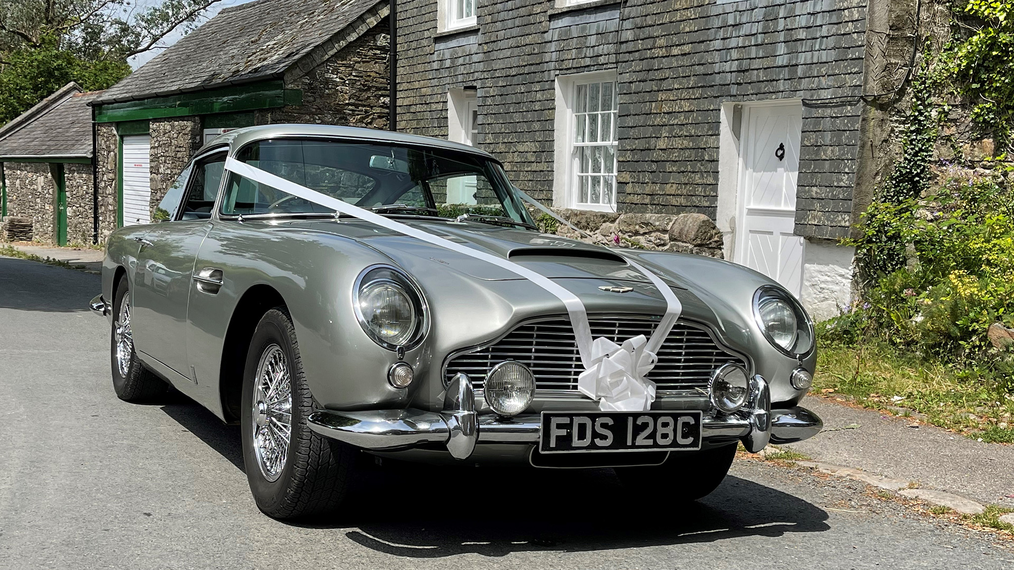 Silver aston Martin DB5 dressed with white ribbons across its bonnet and a white bow on its front grill