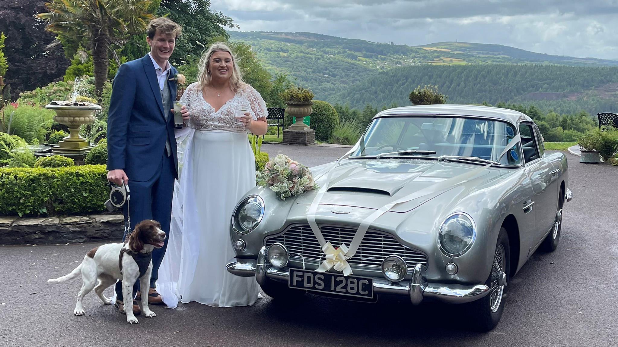 Wedding couple with their dog standing by a classic Aston Martin DB5 in silver