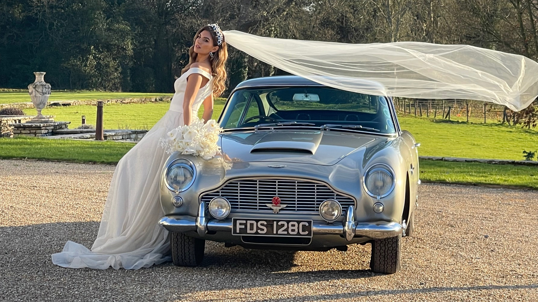 Bride in her white wedding dress having photos taken with a classic Aston Martin DB5