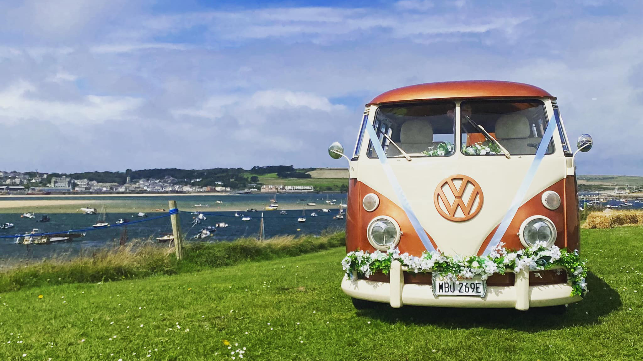 full front view of a classic volkswagen campervan on top of a hill with Cornwall sea side in the background