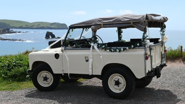 Left view of a classic Land Rover with side windows open on top of a hill on Devon Sea coast