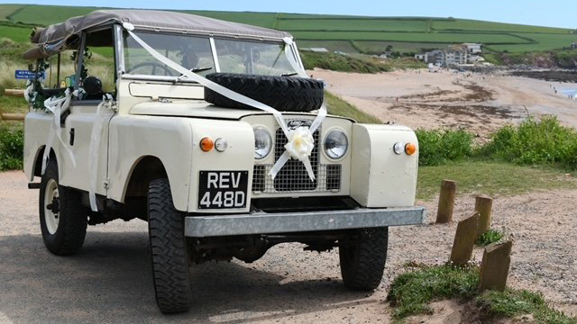 Classic Land Rover decorated with white wedding ribbons and bows