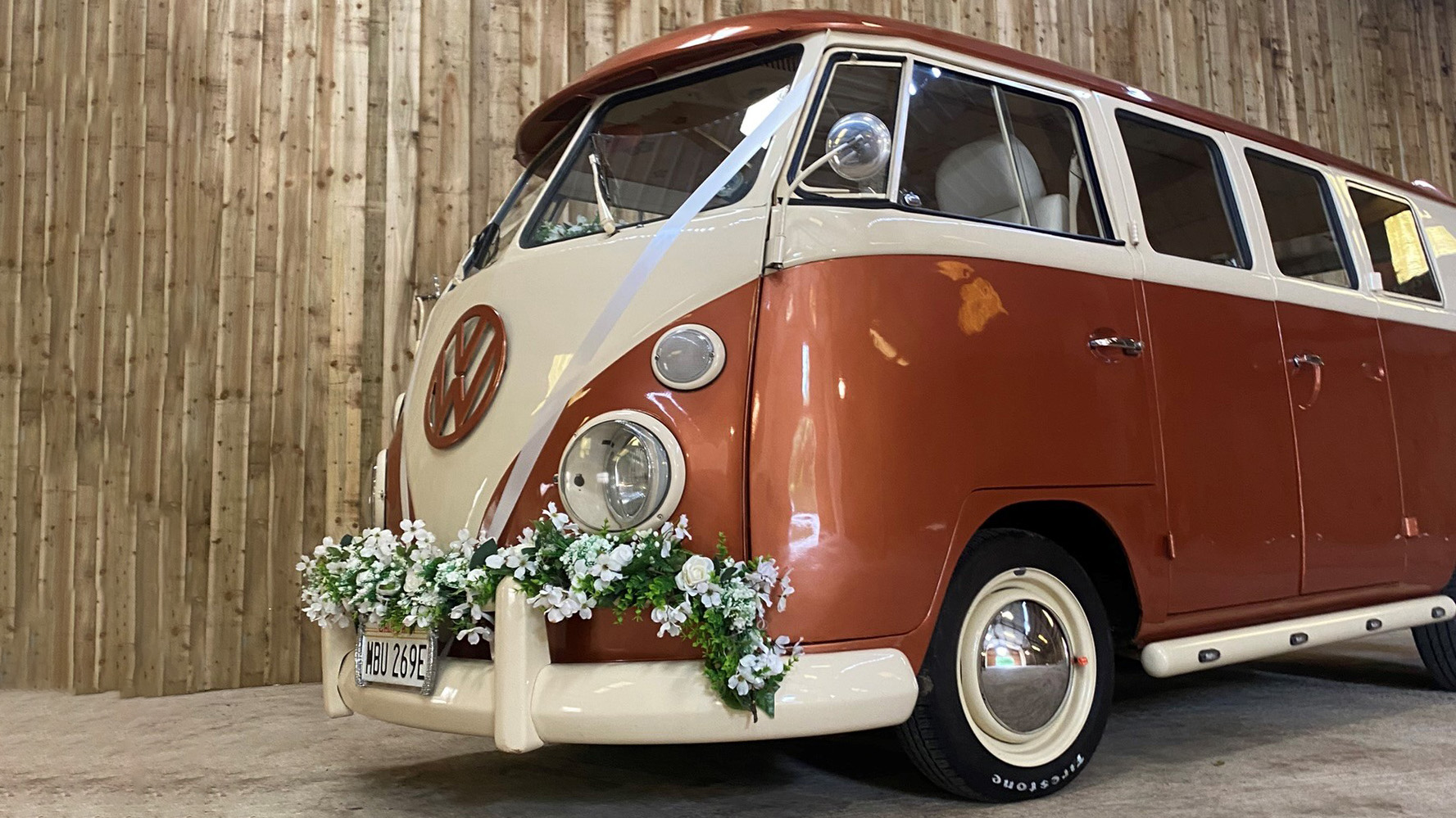 Front left view of a classic Volkswagen campervan in two tone Orange and white with white wedding ribbons