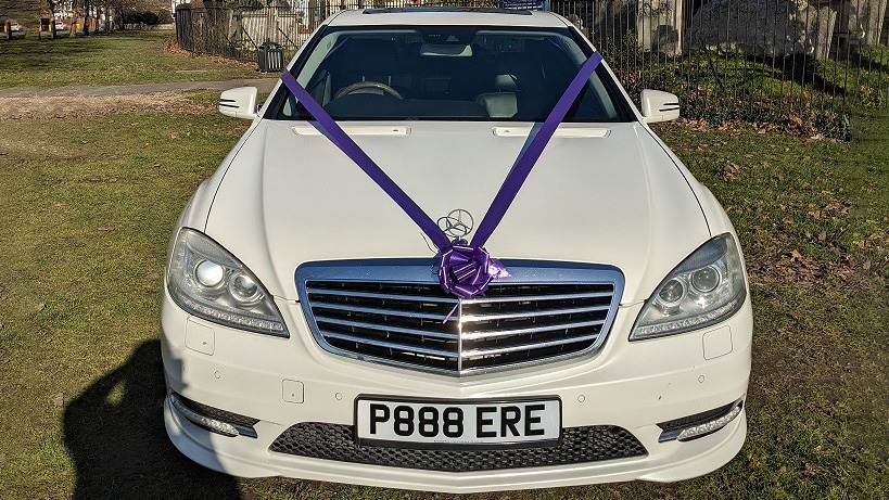 Front view of White Modern Mercedes with purple ribbons and bows