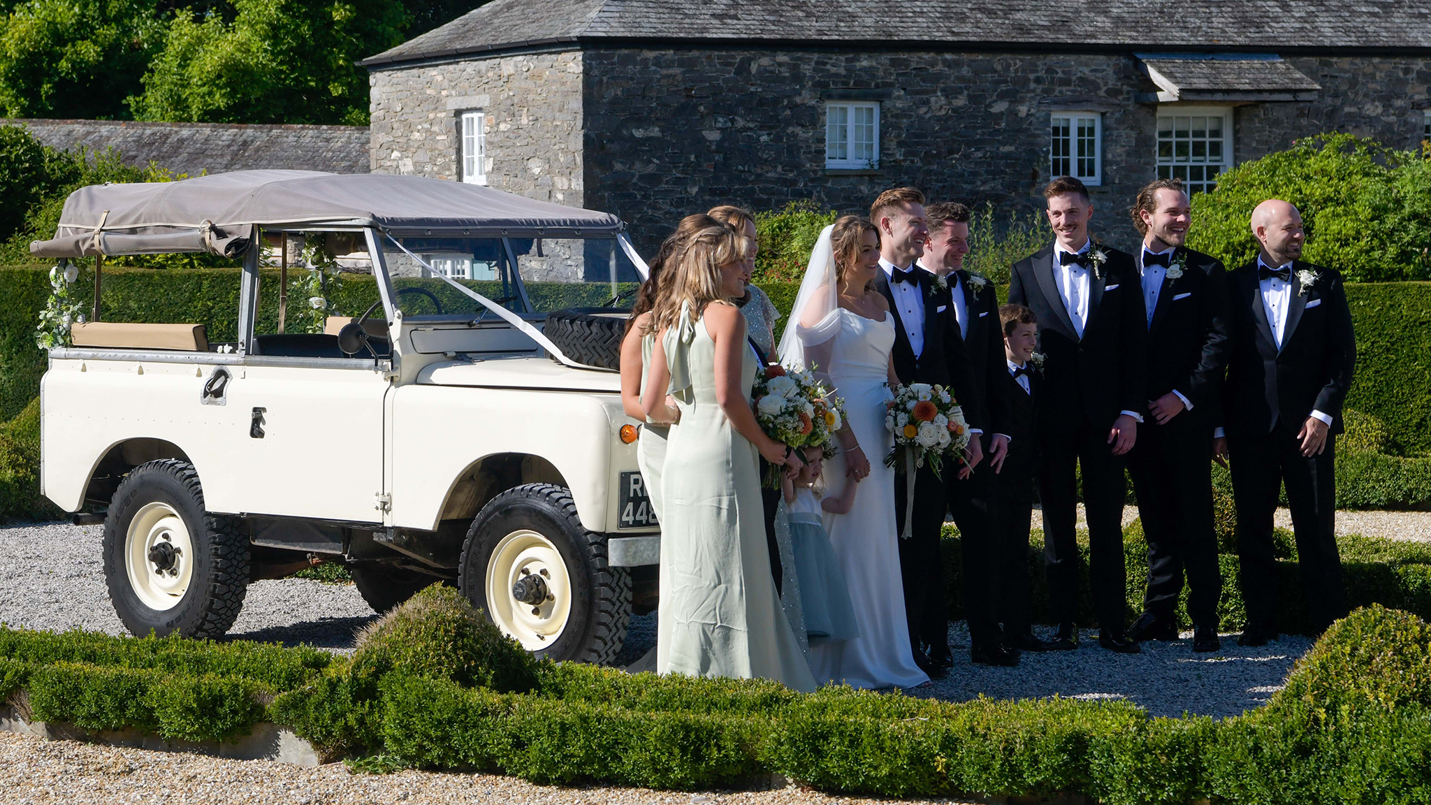 Bride and Groom with Groomsmen and Bridesmaids standing in front of a Classic Land Rover