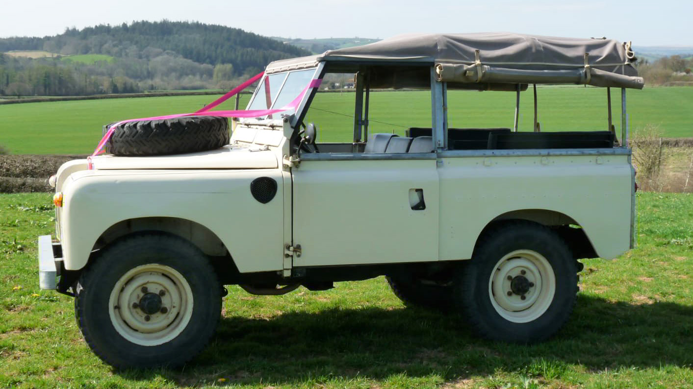 left side view of a Classic Land Rover with pink wedding ribbons