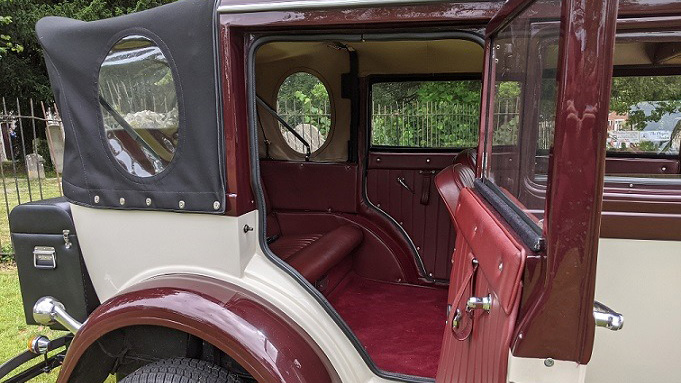 rear passenger door open showing burgundy carpet and leather seats and black soft top roof closed