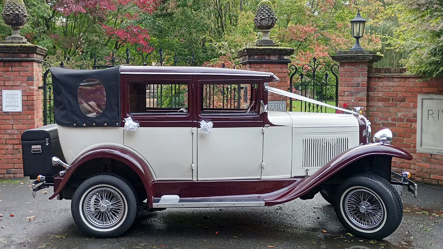 vintage Badsworth wedding car in Ivory with Burgundy wheel arches and roof wth black soft top roof close decorated with ivory ribbons and bows on door handles and rear black picnic trunk