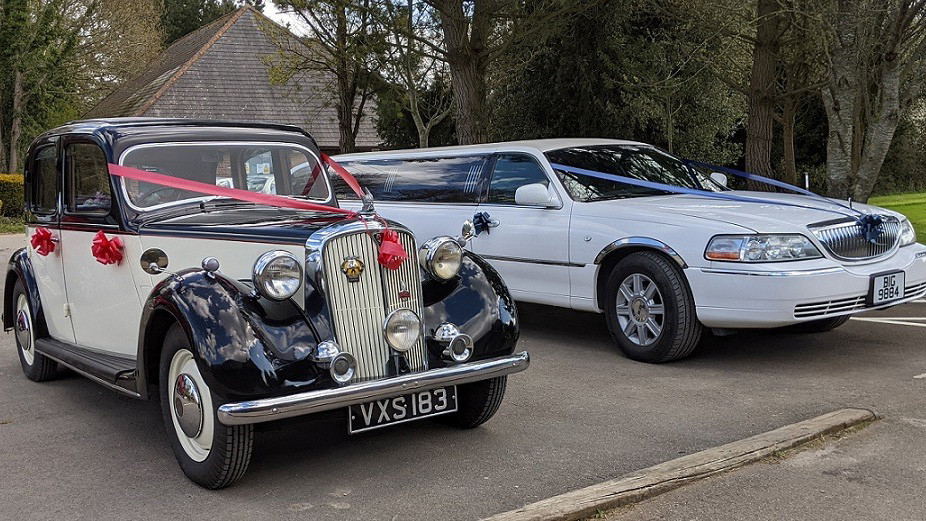 vintage Rover p3 in Black and ivory decorated with Red ribbons and Bows on door handles parked next to a white stretched limousine