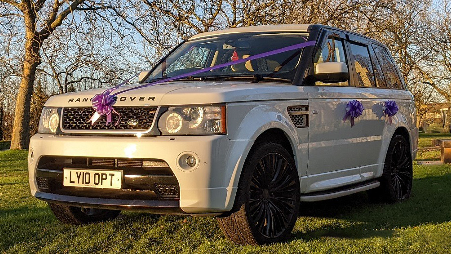 Left front view of white range rover wedding car with purple ribbons and bows