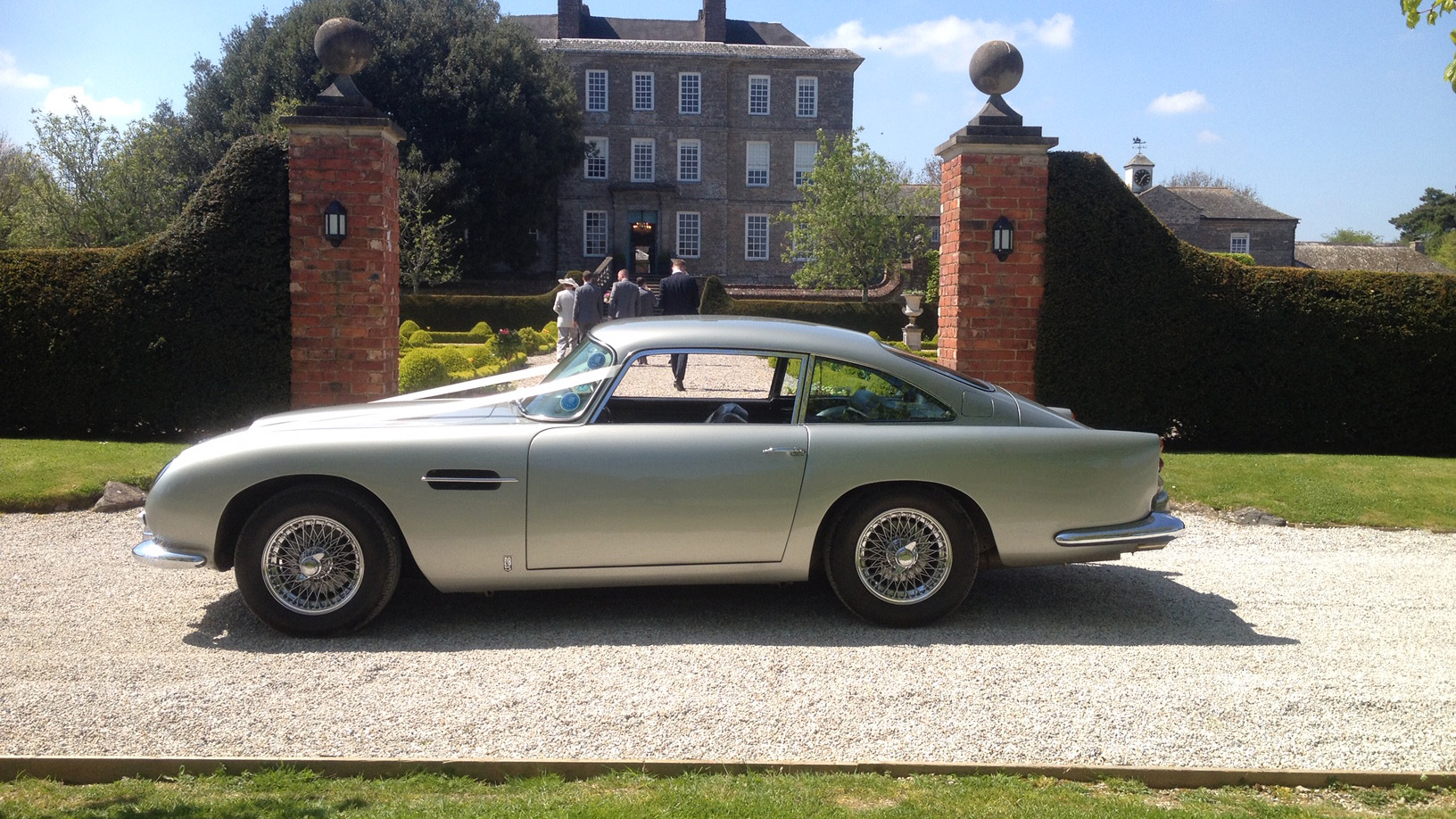 Left side view of a classic Aston Martin DB5 parked in front of a wedding venue