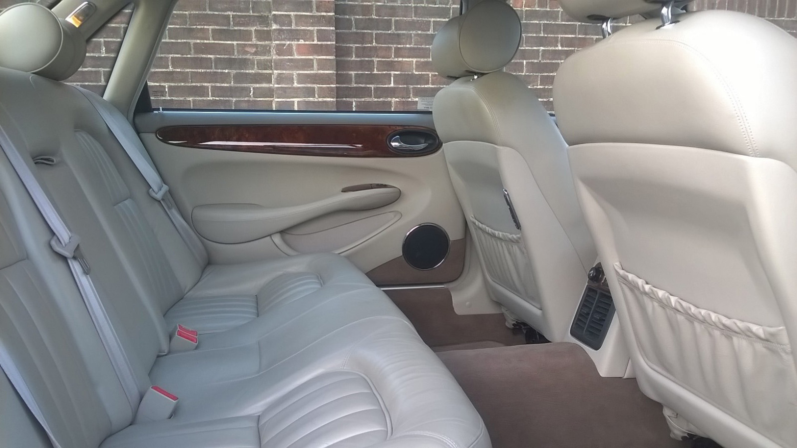 Rear cream leather interior inside a Jaguar with wooden features on top of the door cards and cream carpet