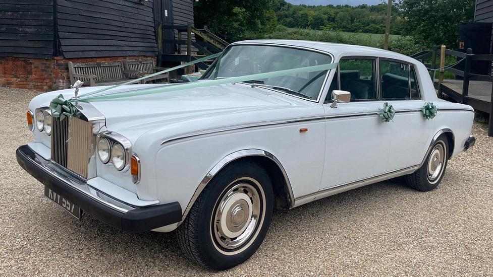 White classic Rolls-Royce silver Shadow 2 with black front bumpers decorated with sage green wedding ribbons and bows