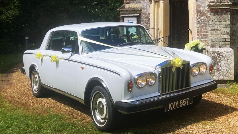 Classic Rolls-Royce silver shadow dressed with Ivory wedding ribbons, twin front head lights switched on parked in front of a church