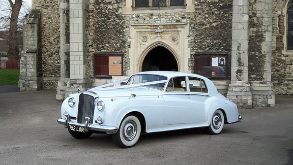 Classic White Bentley decorated with wedding ribbons in front of a church