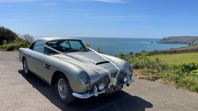 Silver classic Aston Martin DB5 decorated with white wedding ribbons parked on devon south sea coast