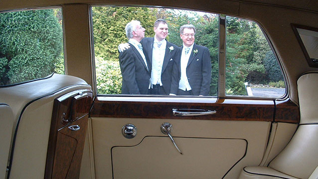 Photo taken frominside a classic Bentley looking at Groom and his two groomsmen through the window