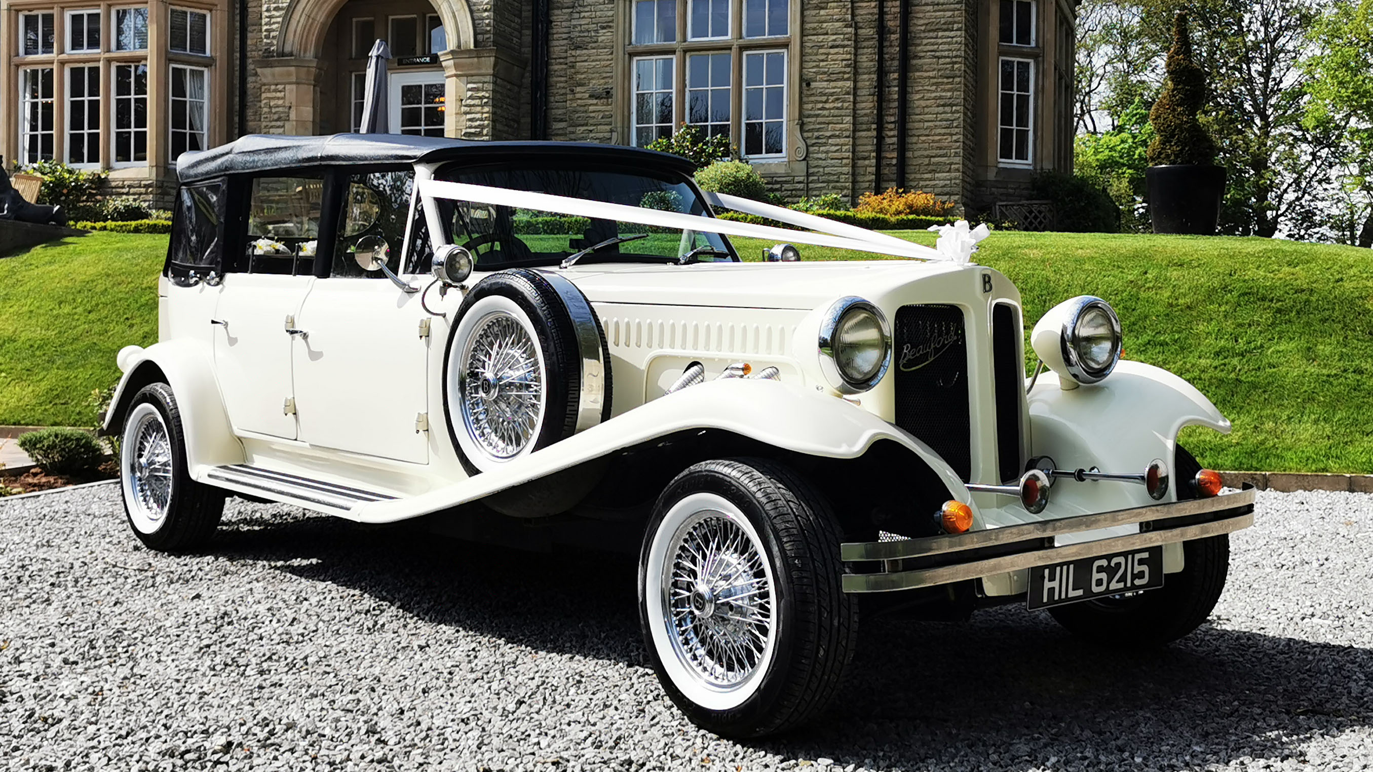 Ivory vintage styl;e Beauford with Black Soft top roof closed parked in the back garden of Arley Hall in Cheshire