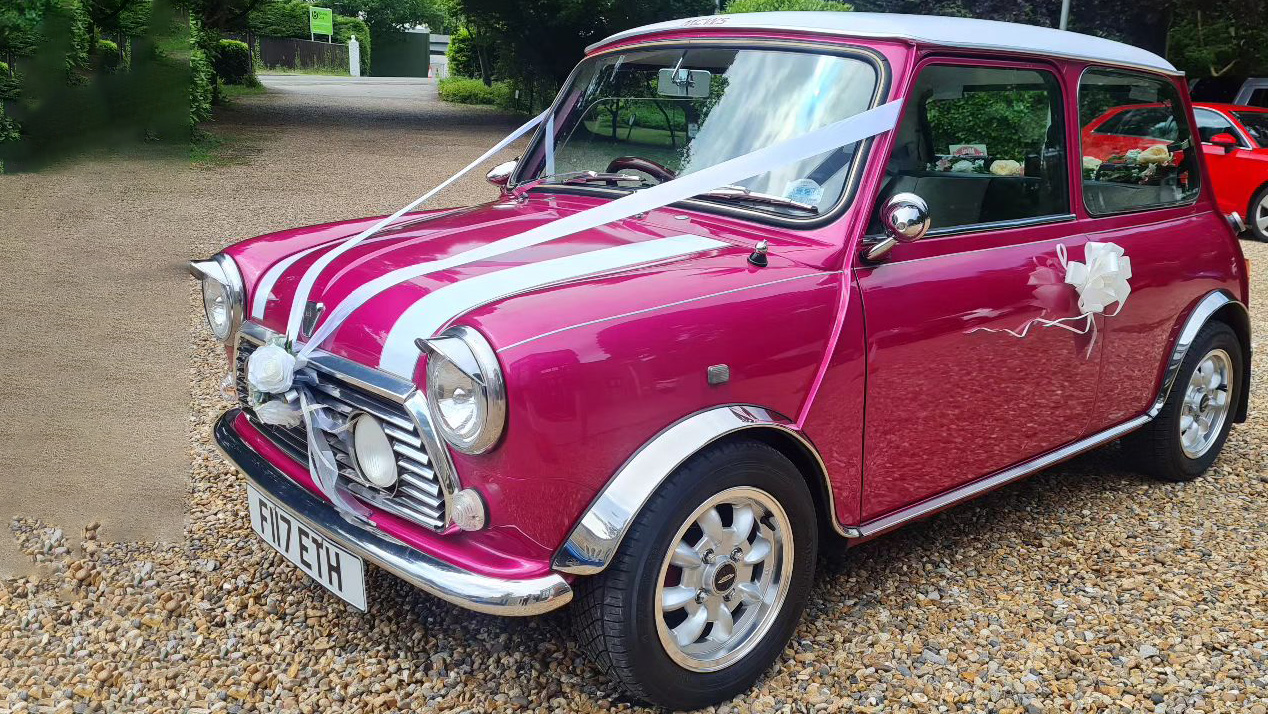 Left side view of Classic Austin Mini in Pink dressed with white wedding ribbons