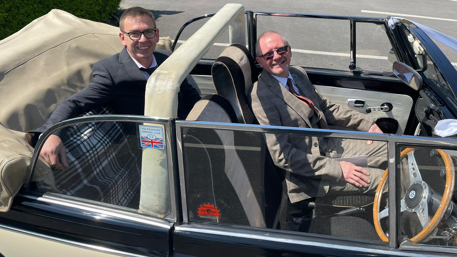 Classic Beetle with convertible roof down showing two smiling passengers seated inside the vehicle.