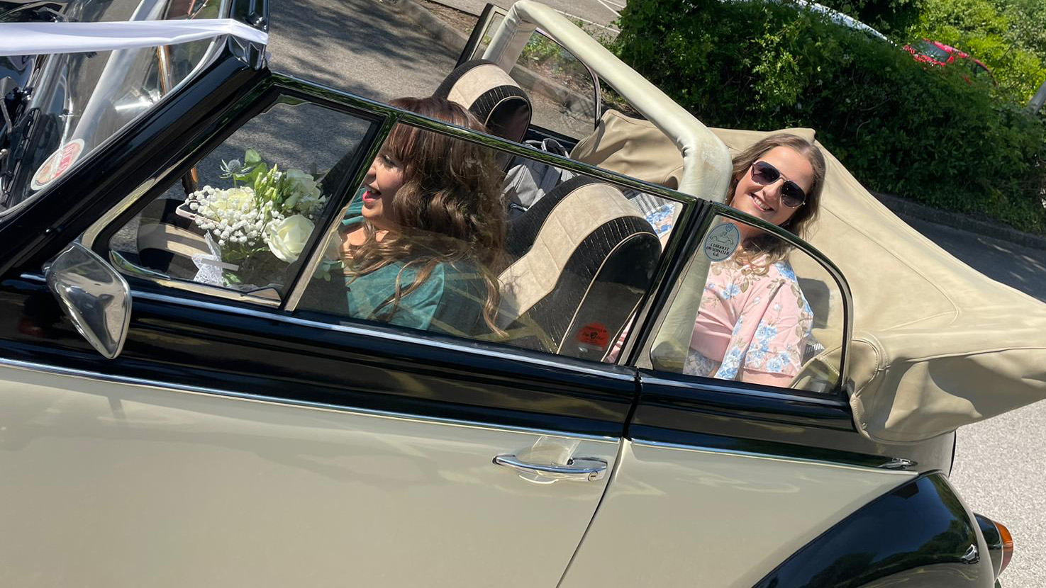 Two passengers seated inside a classic Beetle with roof down