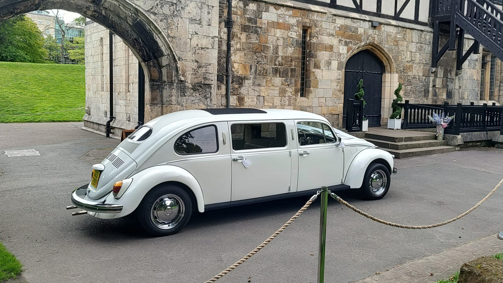 Left side view of Ivory Classic Beetle Stretched limousine parked in front of wedding venue in York.